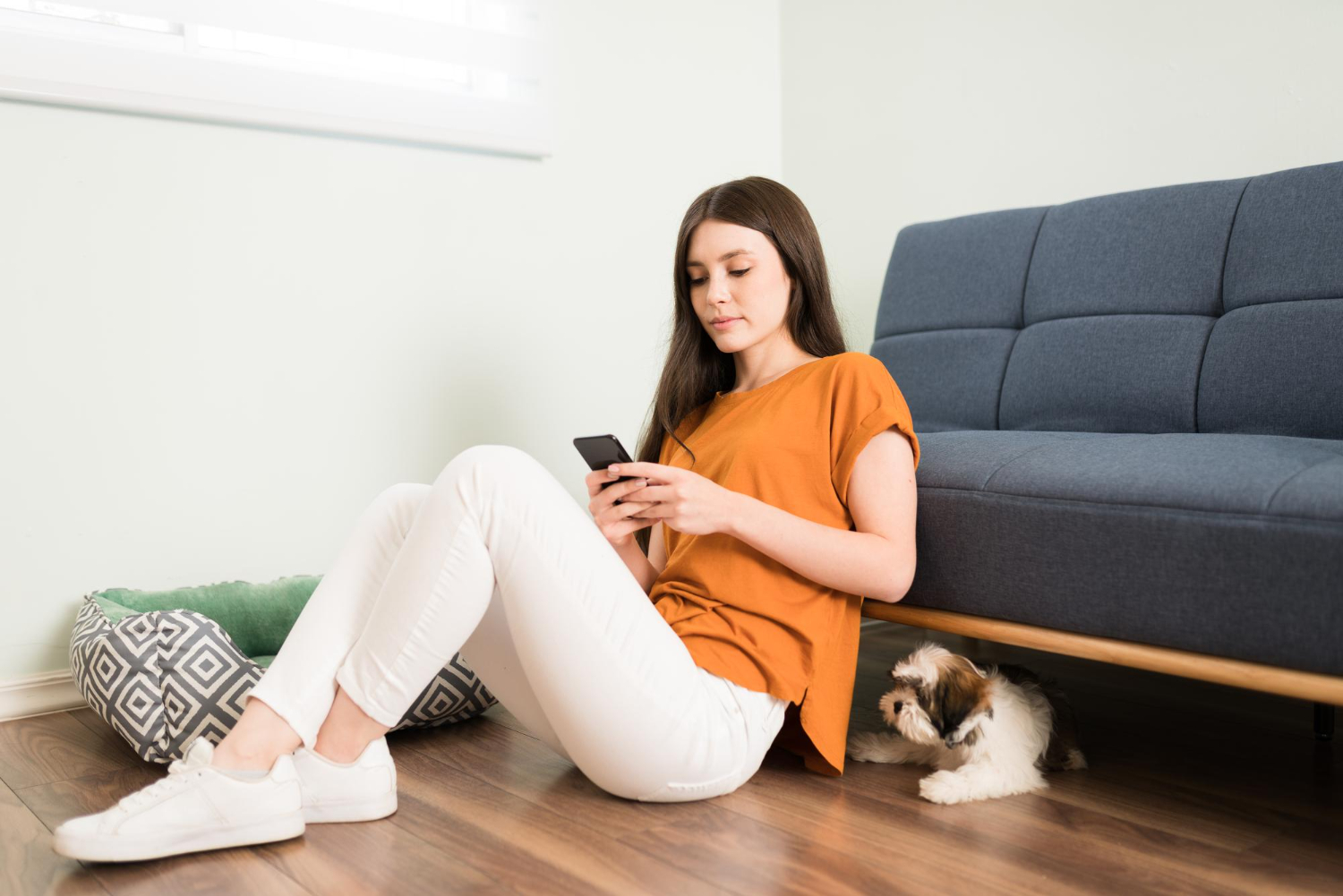 attractive-young-woman-relaxing-at-home-and-texting-on-her-smartphone-while-her-fluffy-lhasa-apso-dog-waits-patiently-to-play