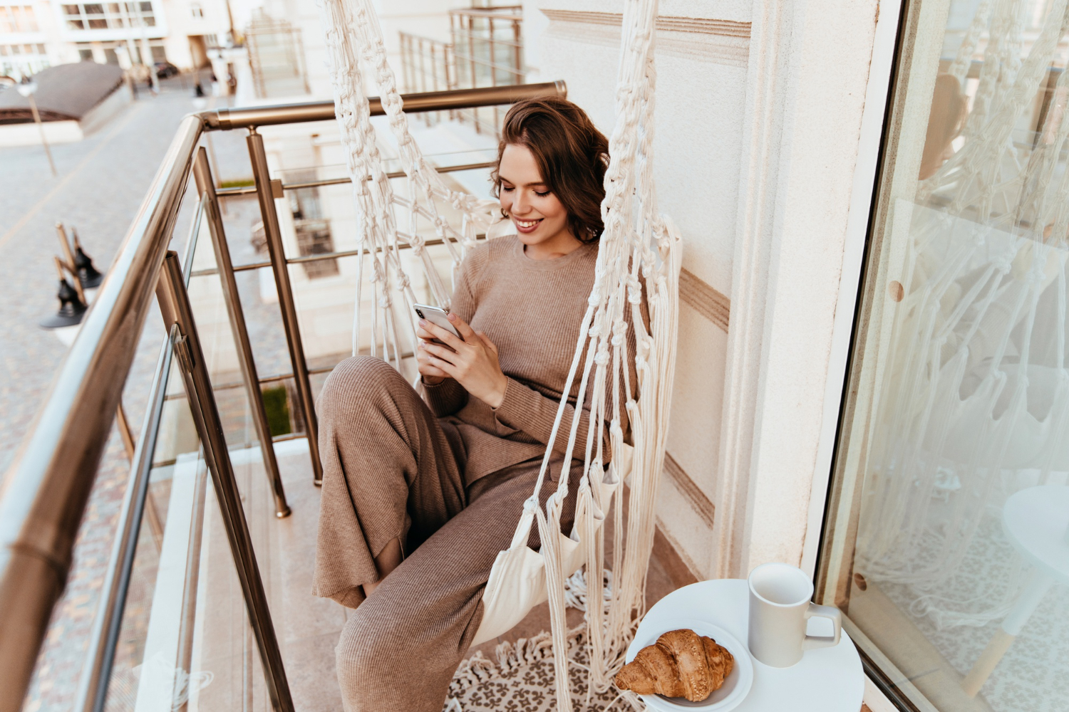 pleasant-girl-texting-message-during-lunch-at-balcony-elegant-young-woman-sitting-at-terrace-with-croissant-and-tea (1)